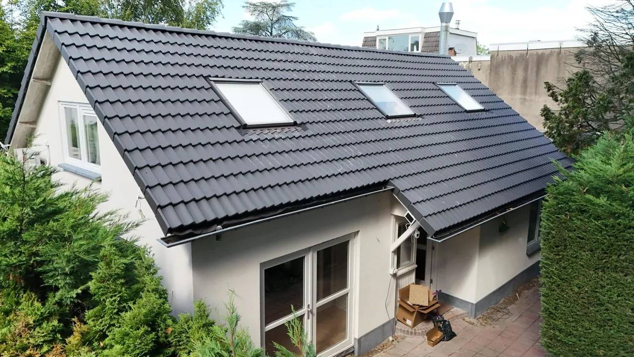 Een wit huis met een nieuw schuin dak van donkergrijze dakpannen en drie dakramen.