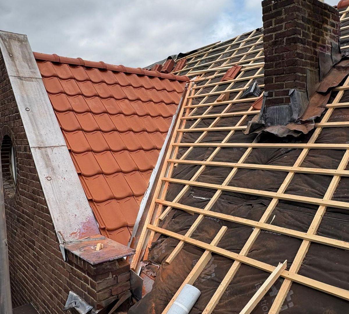 Pannendak in renovatie met verwijderde dakpannen, nieuwe tengels en dampopen folie rond de schoorsteen.