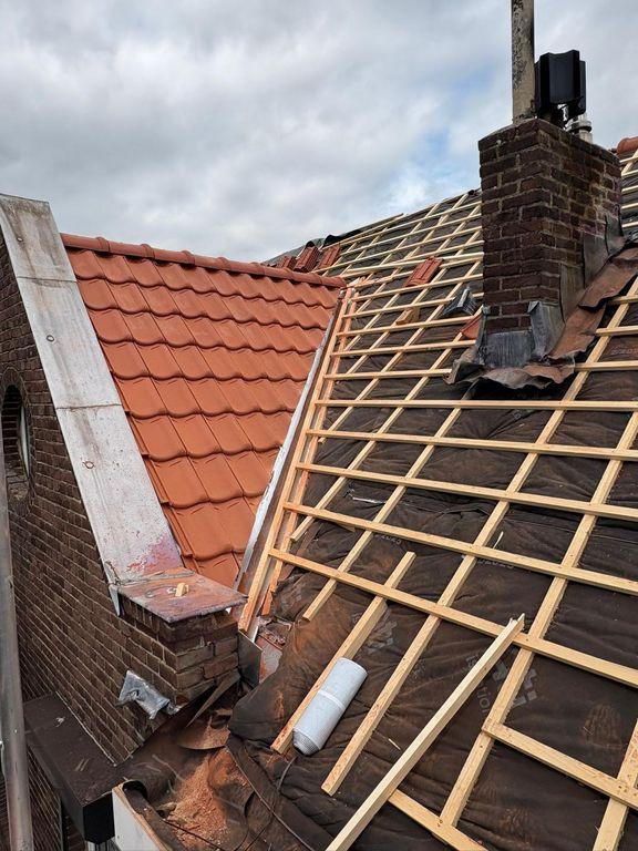 Pannendak in renovatie met verwijderde dakpannen, nieuwe tengels en dampopen folie rond de schoorsteen.