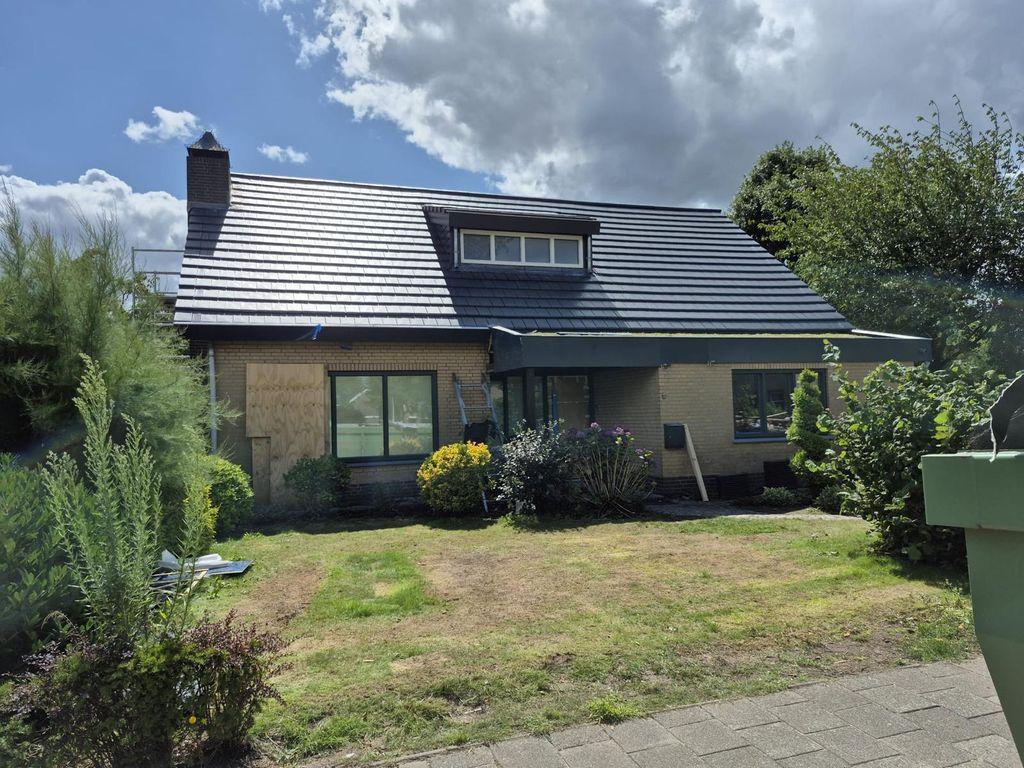 Een vrijstaande woning met een beige bakstenen gevel toont een volledig vernieuwd dak met strakke, antracietgrijze dakpannen en een dakkapel onder een deels bewolkte blauwe lucht.